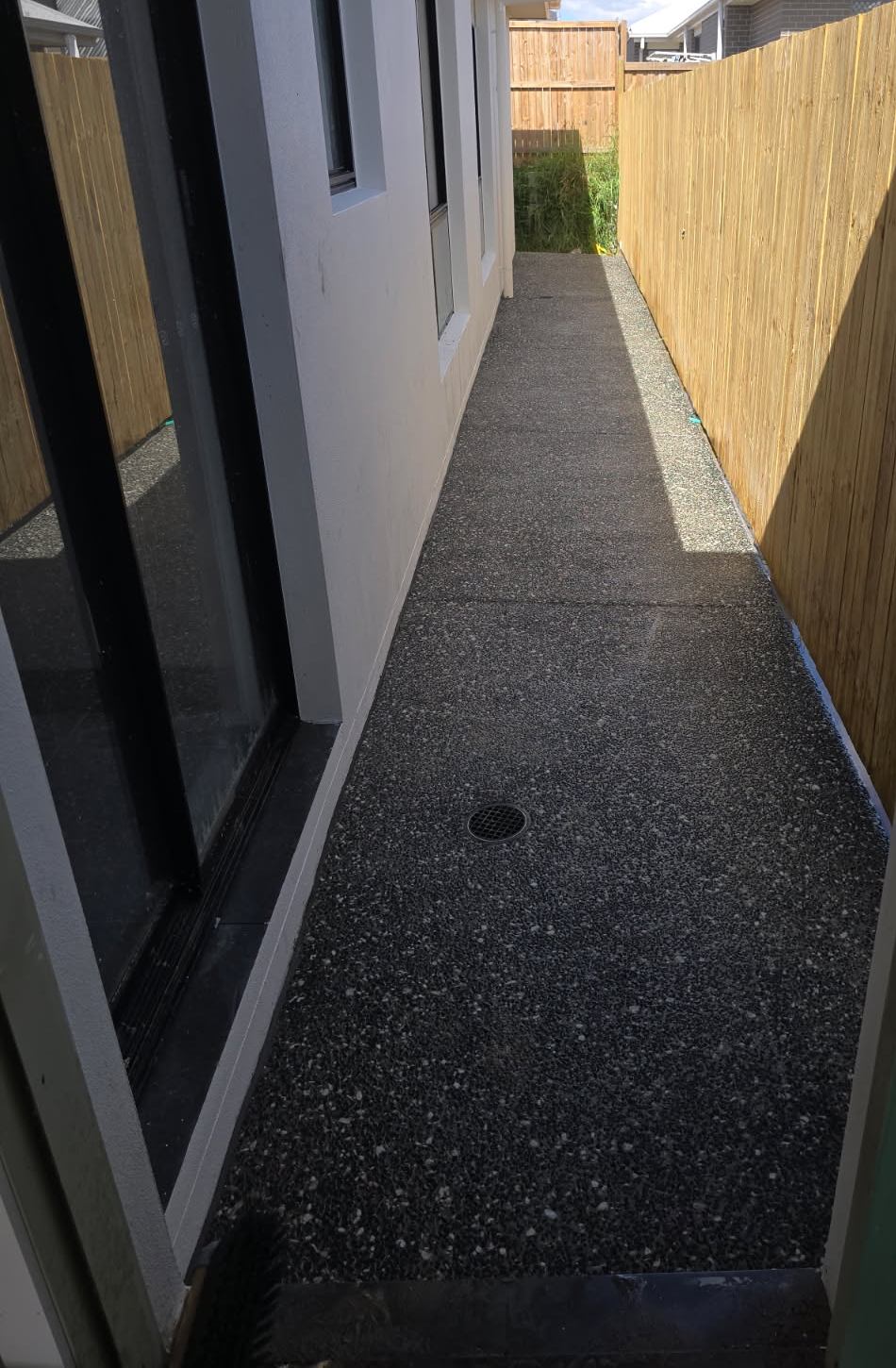 Charcoal exposed aggregate side path between a house and a fence with a grated drain, Sunshine Coast
